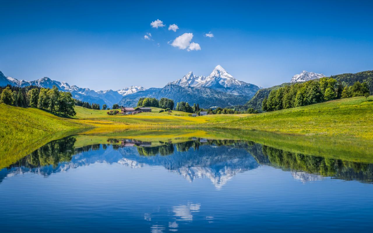 Panoramic view of idyllic summer landscape in the Alps with clear mountain lake and fresh green mountain pastures in the background