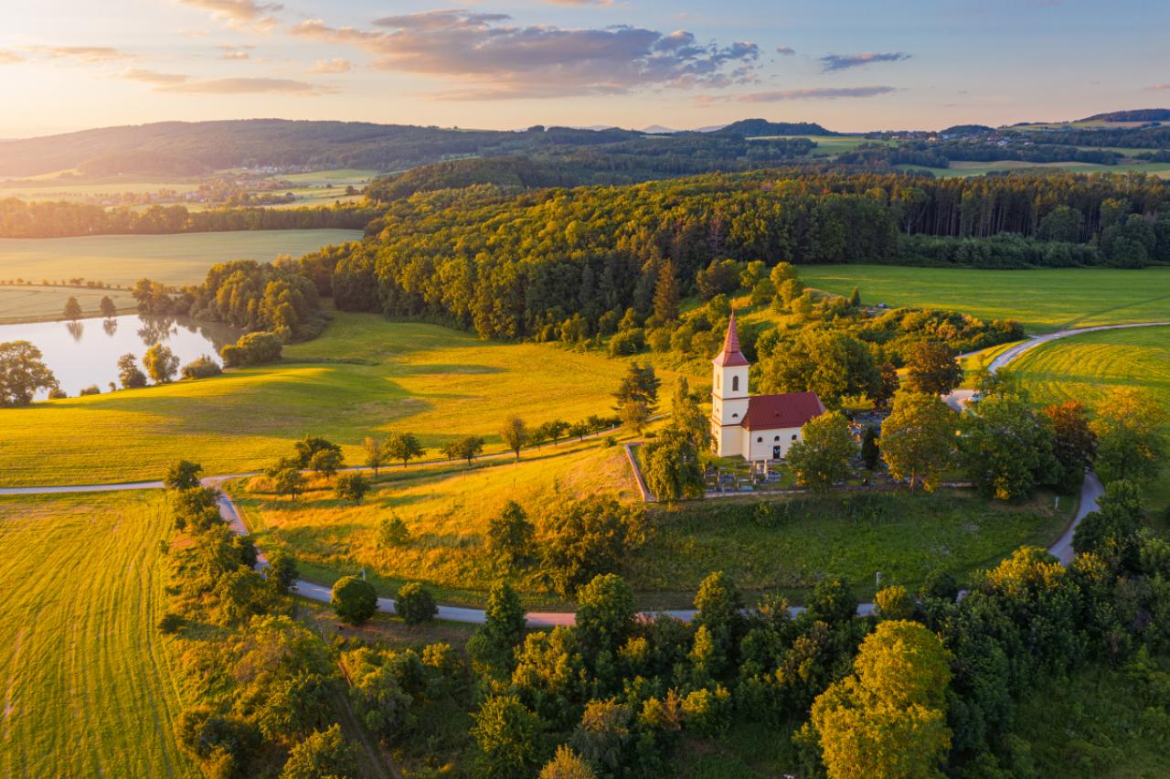 Church on the hill with sunlit summer landscape from above. Bysicky church near SPA town Lazne Belohrad, Czech Republic. Sunset gold light.