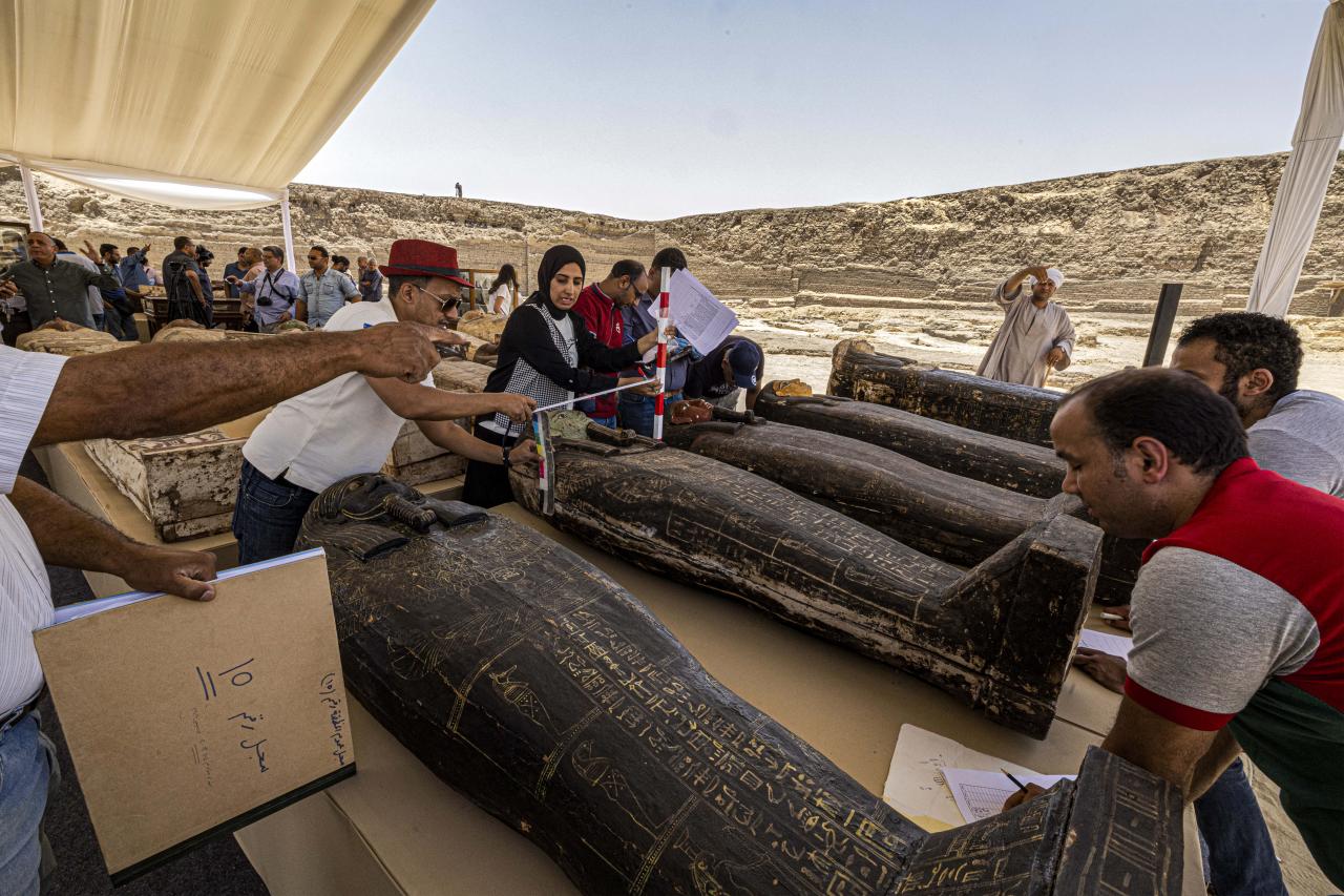 Archaeologists measure the length to register one of the sarcophaguses found in a cache dating to the Egyptian Late Period (around the fifth century BC), discovered by a mission headed by Egypt's Supreme Council of Antiquities, at the Bubastian cemetery at the Saqqara necropolis, southwest of Egypt's capital on May 30, 2022. - Egypt on May 30 unveiled a cache of 150 bronze statues depicting various gods and goddesses including "Bastet, Anubis, Osiris, Amunmeen, Isis, Nefertum and Hathor," along with 250 sarcophagi at the Saqqara archaeological site south of Cairo, the latest in a series of discoveries in the area. (Photo by Khaled DESOUKI / AFP)