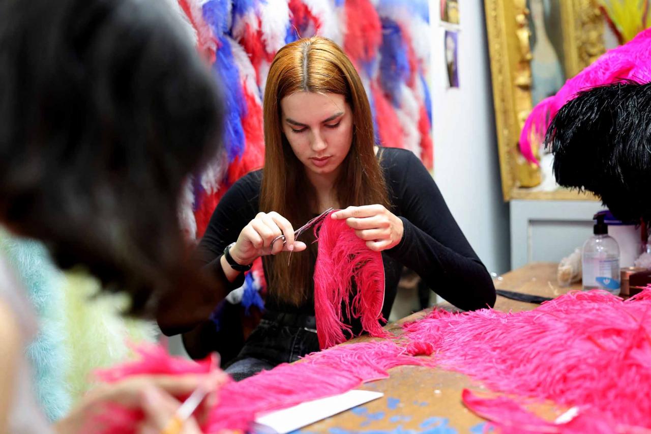 An assistant of Dominique De Roo, official feather craftsman of the Lido cabaret, works on a feather costume inside the workshop, in Paris, on June 1, 2022. - The Lido cabaret, an institution for Parisian night life since 1889, is set to lay off 157 of 184 employees, including its "Bluebell girls" troupe of dancers, announced the new owner, French hotels giant Accor. (Photo by Thomas COEX / AFP)