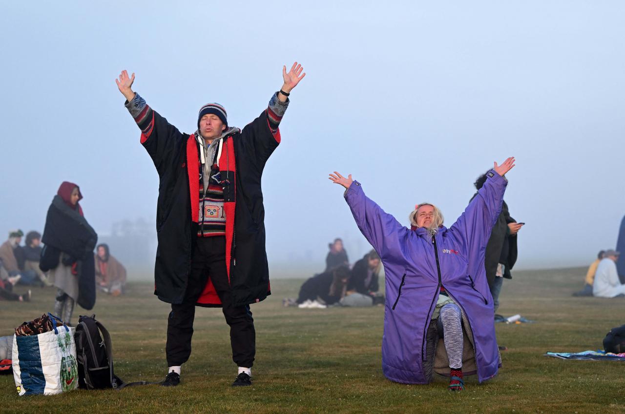 Revelers interact with the stone monument as they celebrate the Summer Solstice as the sun rises at Stonehenge, near Amesbury, in Wiltshire, southern England on June 21, 2022, in a festival, which dates back thousands of years, celebrating the longest day of the year when the sun is at its maximum elevation. - The stone monument -- carved and constructed at a time when there were no metal tools -- symbolises Britain's semi-mythical pre-historic period, and has spawned countless legends. (Photo by Justin TALLIS / AFP)