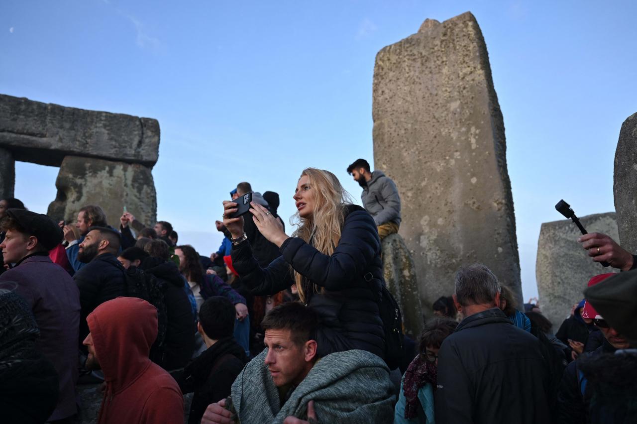 Revelers take photographs as they celebrate the Summer Solstice as the sun rises at Stonehenge, near Amesbury, in Wiltshire, southern England on June 21, 2022, in a festival, which dates back thousands of years, celebrating the longest day of the year when the sun is at its maximum elevation. - The stone monument -- carved and constructed at a time when there were no metal tools -- symbolises Britain's semi-mythical pre-historic period, and has spawned countless legends. (Photo by Justin TALLIS / AFP)