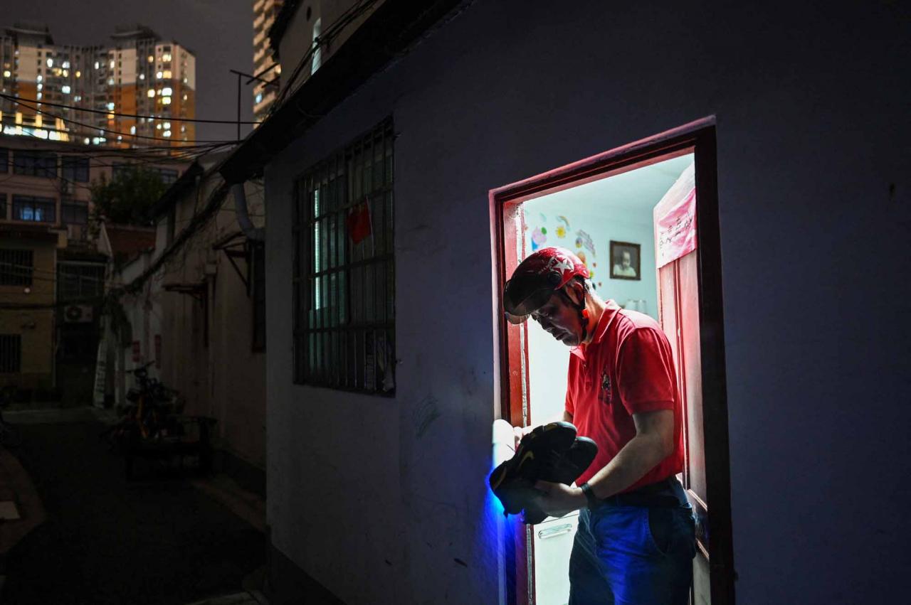 This photo taken on June 30, 2022 shows a resident disinfecting his shoes before entering his home, to be demolished for new development, in the Laoximen neighbourhood of Shanghai's Huangpu district. - Bricked-up doorways, crumbling facades, and a small group of defiant locals: one of Shanghai's oldest neighbourhoods is barely clinging to life as the city presses ahead with demolition and redevelopment plans. (Photo by Hector RETAMAL / AFP)