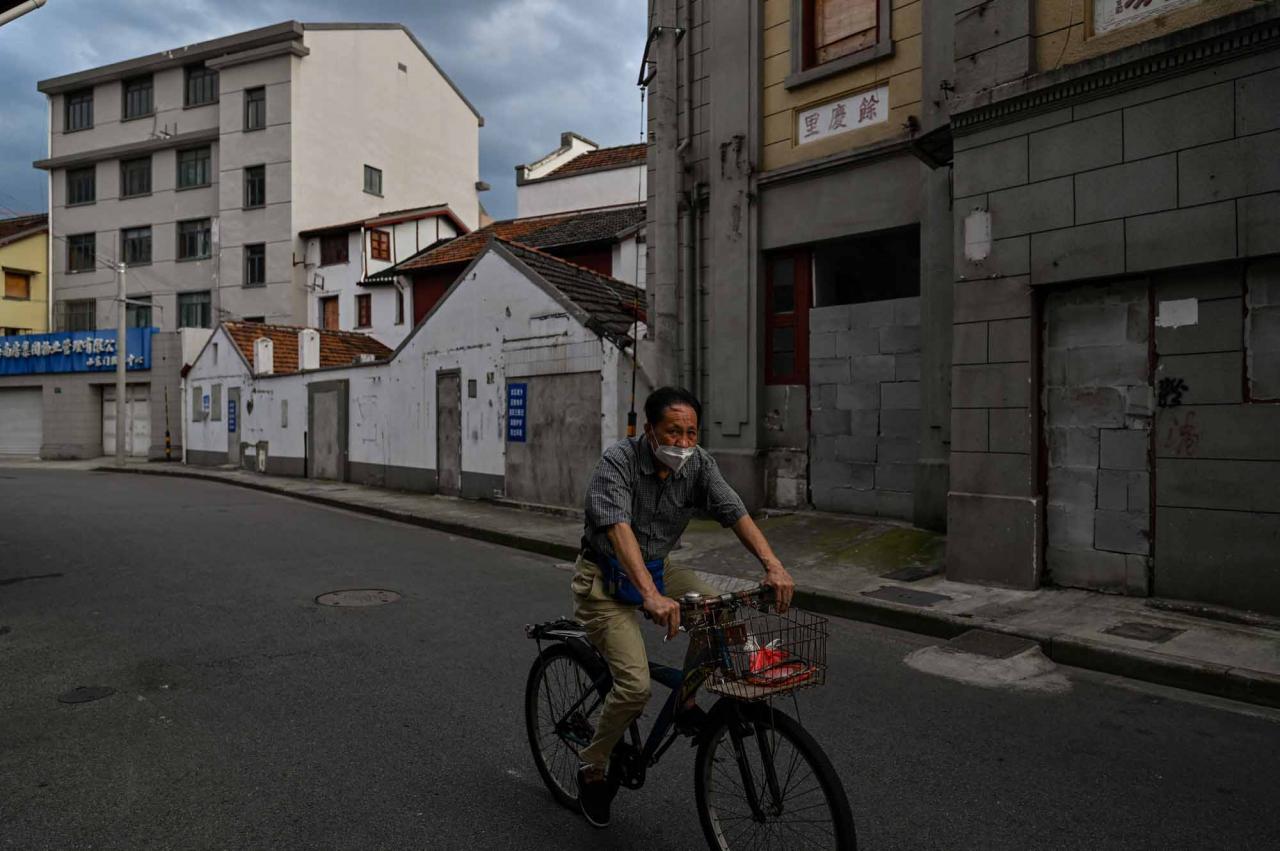 This photo taken on June 22, 2022 shows a man riding a bicycle past sealed buildings marked for demolition in the Laoximen neighbourhood of Shanghai's Huangpu district. - Bricked-up doorways, crumbling facades, and a small group of defiant locals: one of Shanghai's oldest neighbourhoods is barely clinging to life as the city presses ahead with demolition and redevelopment plans. (Photo by Hector RETAMAL / AFP)