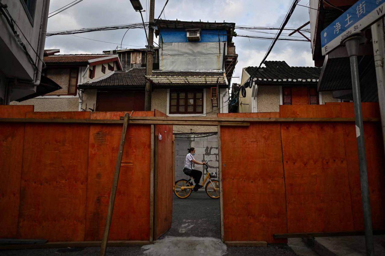 This photo taken on June 22, 2022 shows a woman riding a bicycle past sealed buildings marked for demolition in the Laoximen neighbourhood of Shanghai's Huangpu district. - Bricked-up doorways, crumbling facades, and a small group of defiant locals: one of Shanghai's oldest neighbourhoods is barely clinging to life as the city presses ahead with demolition and redevelopment plans. (Photo by Hector RETAMAL / AFP)