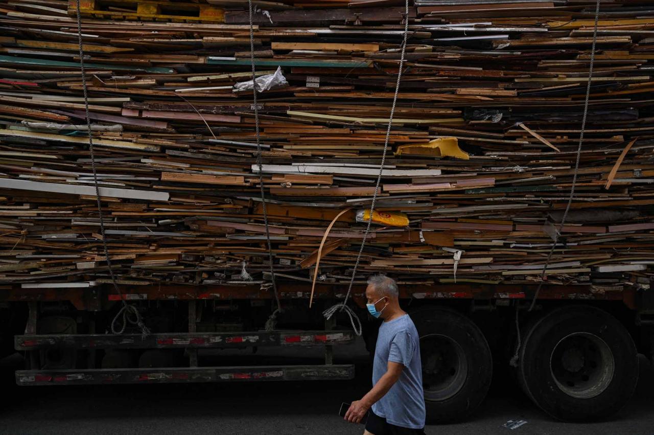 This photo taken on June 22, 2022 shows a man walking past a truck loaded with timber from demolished houses in the Laoximen neighbourhood of Shanghai's Huangpu district. - Bricked-up doorways, crumbling facades, and a small group of defiant locals: one of Shanghai's oldest neighbourhoods is barely clinging to life as the city presses ahead with demolition and redevelopment plans. (Photo by Hector RETAMAL / AFP)