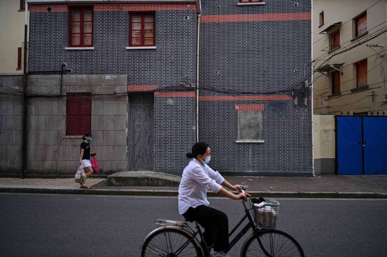 This photo taken on June 22, 2022 shows people cycling and walking past a sealed building marked for demolition in the Laoximen neighbourhood of Shanghai's Huangpu district. - Bricked-up doorways, crumbling facades, and a small group of defiant locals: one of Shanghai's oldest neighbourhoods is barely clinging to life as the city presses ahead with demolition and redevelopment plans. (Photo by Hector RETAMAL / AFP)