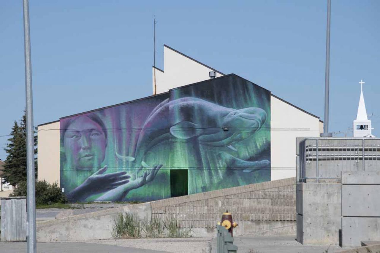This photograph taken on August 11, 2022, shows a mural by artist Charlie Johnson depicting beluga whales and an indigenous woman on the side of a building in Churchill, northern Canada. - Under the slightly murky surface where the waters of the Churchill River meet Hudson Bay, the belugas have a great time under the amazed eye of tourists, several thousand of whom come every year to the small town of Churchill in northern Manitoba to observe them.  In August, at the mouth of the Churchill River, in this area at the gateway to the Canadian Arctic, which is warming three to four times faster than the rest of the planet, temperatures fluctuate between 10 and 20°. (Photo by Olivier MORIN / AFP) / RESTRICTED TO EDITORIAL USE - MANDATORY MENTION OF THE ARTIST UPON PUBLICATION - TO ILLUSTRATE THE EVENT AS SPECIFIED IN THE CAPTION