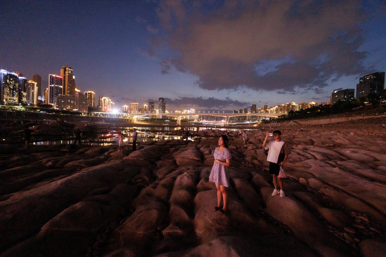 Mensen kijken naar de skyline vanaf de droge rivierbedding van de terugtrekkende Jialing rivier, een zijrivier van de Yangtze, die een recordlaag waterpeil nadert tijdens een regionale droogte in Chongqing, China op 20 augustus, 2022. @Reuters