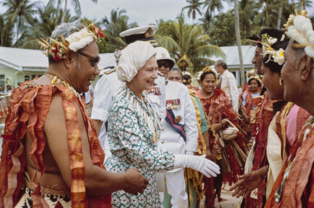 Tuvaluans in traditional dress with British Royal Queen Elizabeth ll, wearing a floral print outfit with white gloves and a hat designed by milliner Frederick Fox, during a visit to Funafuti, Tuvalu, 26th October 1982. The visit was part of the Royal Tour of Australia and the Pacific Islands. (Photo by Tim Graham Photo Library via Getty Images)