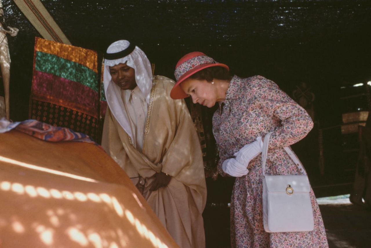 British Royal Queen Elizabeth II, wearing a floral print outfit with a red safari helmet-style hat, with a floral band to match the outfit, during a walkabout with a Saudi guide, location unspecified, in Saudi Arabia, February 1979. The British Royals are on a tour of the Gulf States. (Photo by Tim Graham Photo Library via Getty Images)