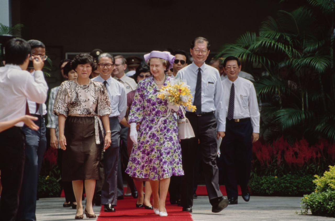 British Royal Queen Elizabeth ll, wearing a lilac, green and white outfit with a Philip Somerville hat, carrying a bouquet of flowers during a visit to Townsville Primary School, part of her visit to Singapore, 10th October 1989. The Royal couple is on a three-day official visit to Singapore, en route to Malaysia, where the Queen opens the Commonwealth Heads of Government Meeting on 18th October. (Photo by Tim Graham Photo Library via Getty Images)