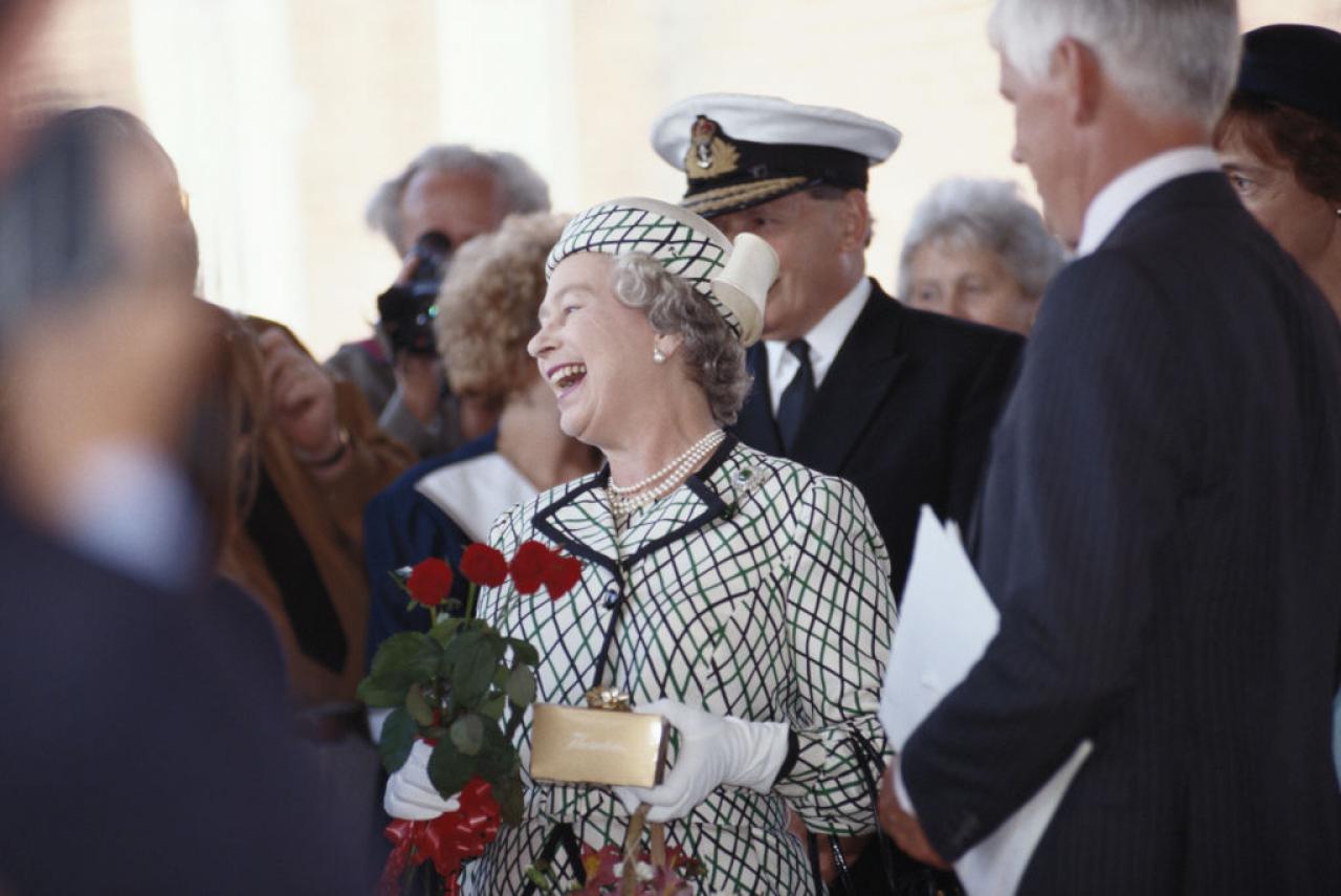 Queen Elizabeth II laughing while holding a small bouquet of flowers before boarding the Royal yacht Britannia in Portsmouth, Hampshire, England, Great Britain, 6 August 1992. Britannia was to leave Portsmouth on a cruise of the Western Isles for the Royal summer holiday.  (Photo by Tim Graham Photo Library via Getty Images)