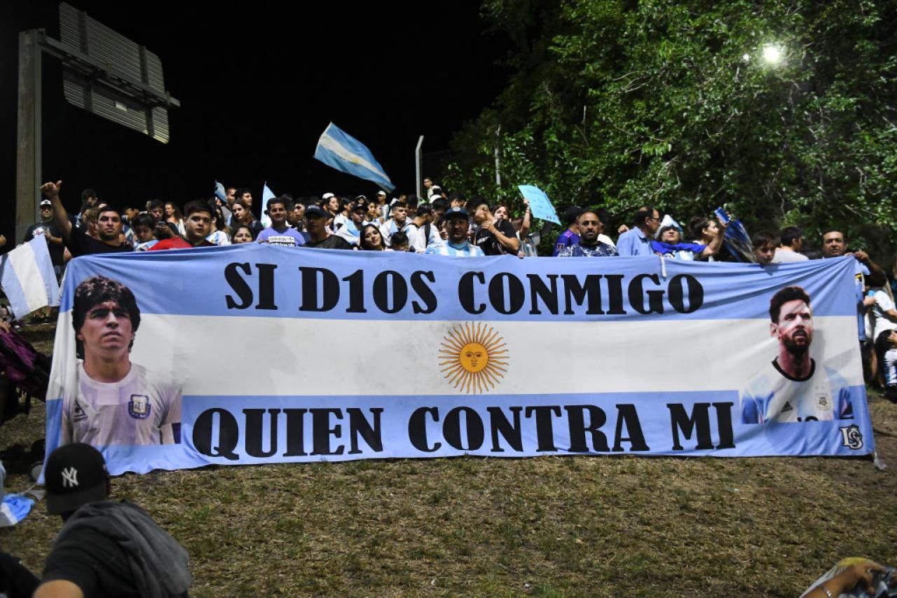 BUENOS AIRES, ARGENTINA - DECEMBER 20: Fans of Argentina display a flag of Lionel Messi and late football legend Diego Maradona before the arrival of the Argentina men's national football team after winning the FIFA World Cup Qatar 2022 on December 20, 2022 in Buenos Aires, Argentina. (Photo by Rodrigo Valle/Getty Images)