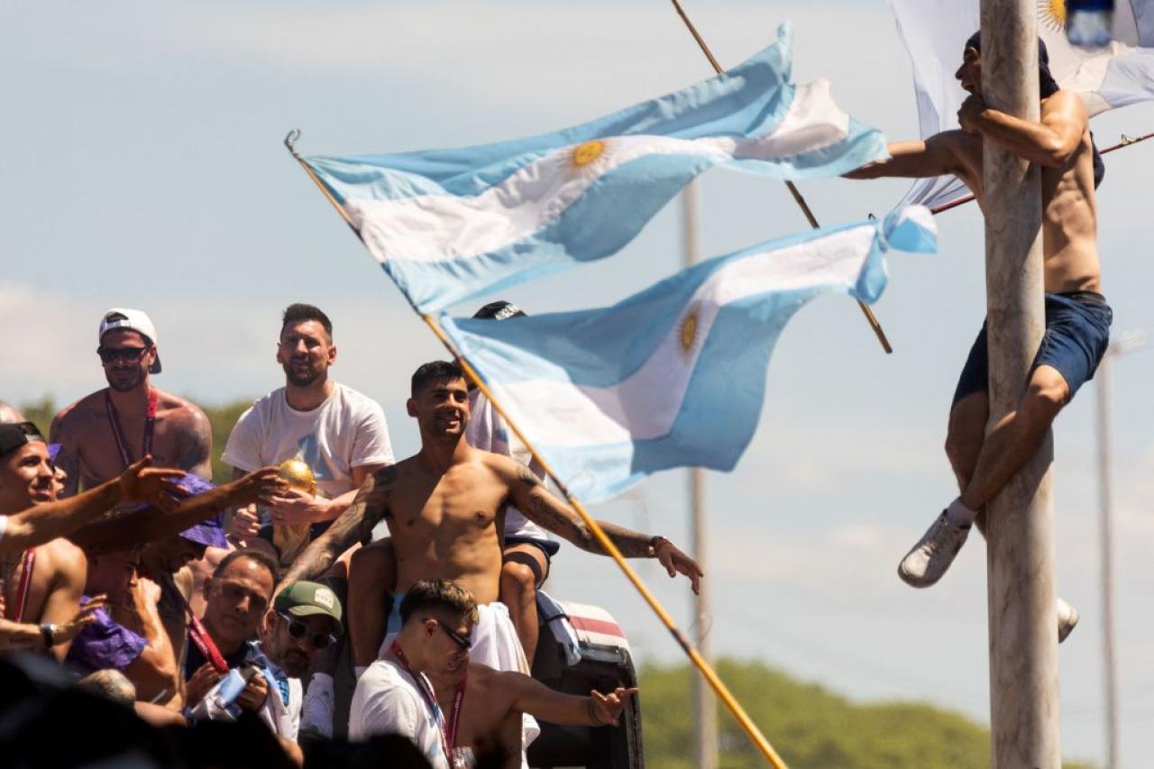 TOPSHOT - A fan of Argentina clinging to a pole cheers as the team parades on board a bus after winning the Qatar 2022 World Cup tournament, in Buenos Aires province, on December 20, 2022. - Millions of ecstatic fans are expected to cheer on their heroes as Argentina's World Cup winners led by captain Lionel Messi began their open-top bus parade of the capital Buenos Aires on Tuesday following their sensational victory over France. (Photo by TOMAS CUESTA / AFP) (Photo by TOMAS CUESTA/AFP via Getty Images)