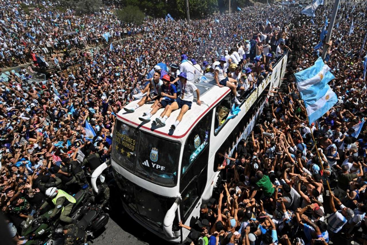 TOPSHOT - Fans of Argentina cheer as the team parades on board a bus after winning the Qatar 2022 World Cup tournament in Buenos Aires, Argentina on December 20, 2022. - Millions of ecstatic fans are expected to cheer on their heroes as Argentina's World Cup winners led by captain Lionel Messi began their open-top bus parade of the capital Buenos Aires on Tuesday following their sensational victory over France. (Photo by Luis ROBAYO / AFP) (Photo by LUIS ROBAYO/AFP via Getty Images)