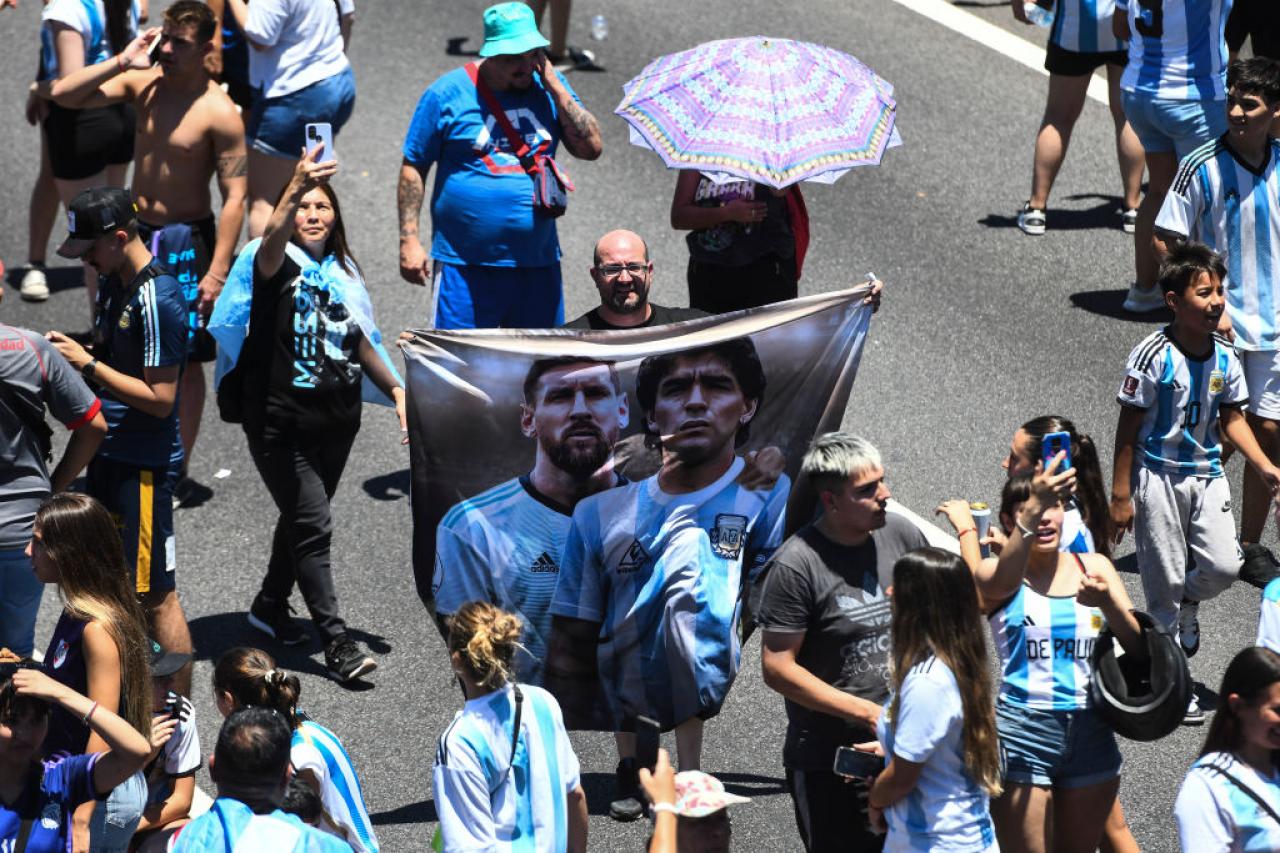BUENOS AIRES, ARGENTINA - DECEMBER 20: A fan of Argentina shows a flag of Lionel Messi and late football legend Diego Maradona in General Paz avenue as they wait for the victory parade of the Argentina men's national football team after winning the FIFA World Cup Qatar 2022 on December 20, 2022 in Buenos Aires, Argentina. Due to security reasons amid the a multitude of fans that collapsed the highways, the route of the open-top bus carrying the Argentina national team for the parade was interrupted. It is estimated more than 4 million fans arrived to the highways and streets. (Photo by Rodrigo Valle/Getty Images)