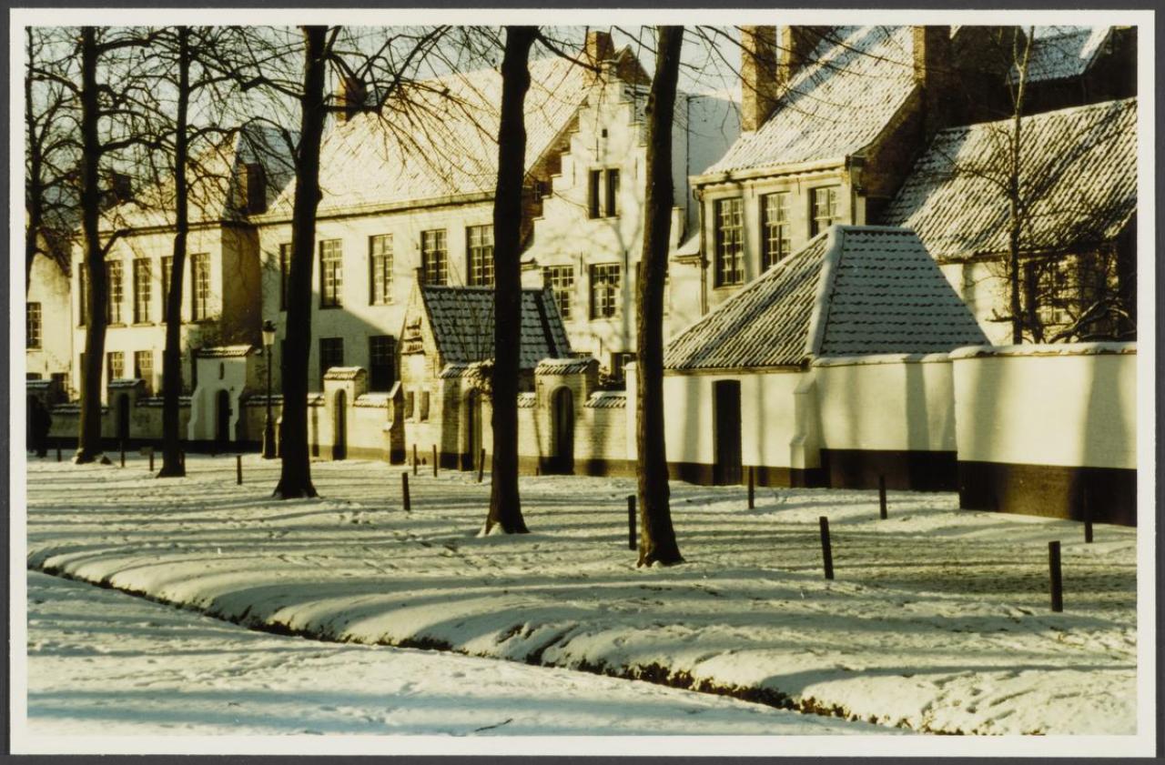 De noordelijke rij huizen van het Brugse begijnhof in de sneeuw. Deze huizen kregen in 1937-39 een voortuintje dat van het plein gescheiden werd met een muur met korfboogpoortjes. In deze muur zien we ook het kleine huisje gebruikt als duiventil.