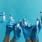 Handen houden vaccin omhoog met blauwe handschoenen op blauwe achtergrond.