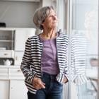 Vrouw op middelhoge leeftijd mijmert terwijl ze door de ruit kijkt.