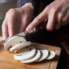 Persoon snijdt paddestoelen op snijplank.