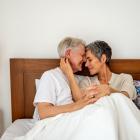 Een ouder koppel knuffelt en toont affectie in bed onder de lakens