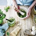 Bovenaanzicht van persoon die pesto maakt met alle ingrediënten ernaast.