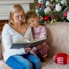 Meisje met oma die thuis onder de kerstboom een ​​boek leest, zittend op de bank.
