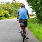 Oudere man fiets op asfalt omringd door bomen