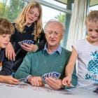 grootvader met drie kleinkinderen spelen een spel kaarten.