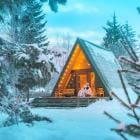 Een vrouw zit tijdens de winter in een A-frame hutje in een besneeuwd bos.