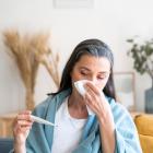 Een zieke vrouw van middelbare leeftijd snuit in een zakdoek terwijl ze haar temperatuur meet.