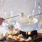 2 stukjes brood die in kaasfondue worden gedipt omringd door wijn en olijven.