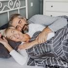 Koppel op middelbare leeftijd ligt in bed terwijl ze glimlachen.