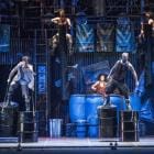 Leden van STOMP in actie op podium, staand op grote metalen tonnen.