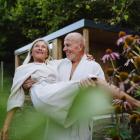 Ouder koppel in witte badjassen in een tuin terwijl de man de vrouw draagt