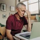 Oudere man zit peinzend achter zijn laptop.