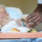 Oude man in ziekenhuisbed grijpt naar glas water.