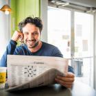 Man van middelbare leeftijd leest krant terwijl hij bril vasthoudt.