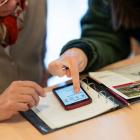 Jongere vrouw wijst op de smartphone aan hoe oudere vrouw deze moet gebruiken.