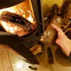 Persoon legt houtblok in de brandende kachel.