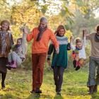 Een vrolijke familie met meerdere generaties die op een lentedag in de natuur geniet, terwijl ze elkaars hand vasthouden en met de kleintjes schommelen.