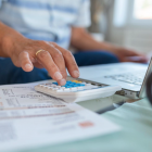 Vrouw maakt berekeningen met rekenmachine en laptop.