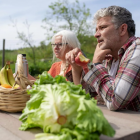 Man en vrouwen zitten aan picknicktafel en eten groenten en fruit.