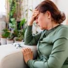 Oudere dame zit in zetel met hoofd in haar hand.