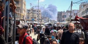 Palestinians crowd a street as smoke billows nearby from Israeli strikes in Rafah in the southern Gaza Strip on May 7, 2024.
