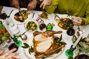 High Angle View Hands Of Friends Talking And Eating Traditional Christmas Turkey Dinner At Table With Red Wine And Candles