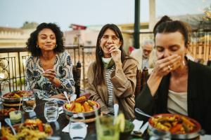 Medium shot of women laughing and savoring traditional Moroccan tajine at scenic rooftop eatery during holiday in Marrakech