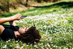 Teenage boy surfing the net while lying down on grass at springtime