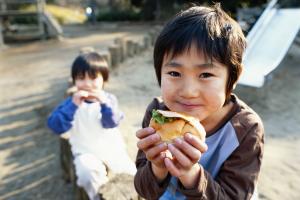 Jongens van vier en zes jaar eten een hamburger op een speelpleintje